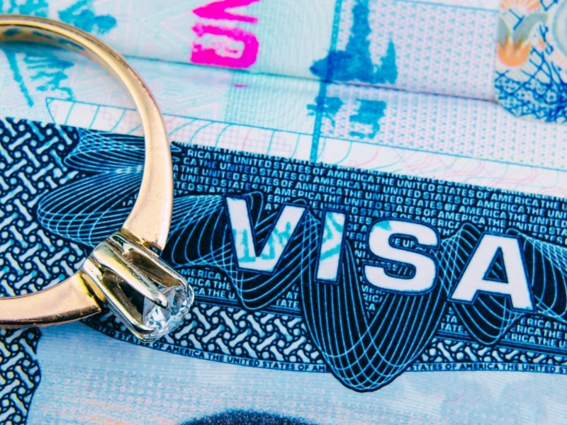 Engagement ring on top of blurred US entry visa sticker in a passport.