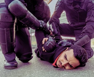 Riot force in protective wear pressing middle eastern man to ground while arresting him during the rally.