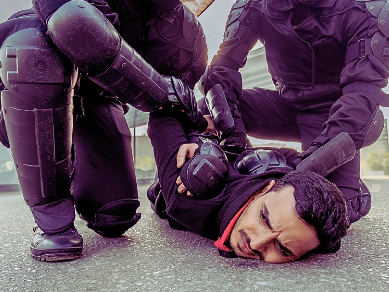 Riot force in protective wear pressing middle eastern man to ground while arresting him during the rally.