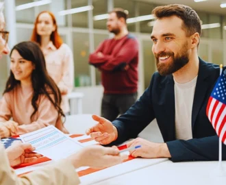 a man with a beard sitting at a registration table, engaging in conversation. Immigration Parole Programs