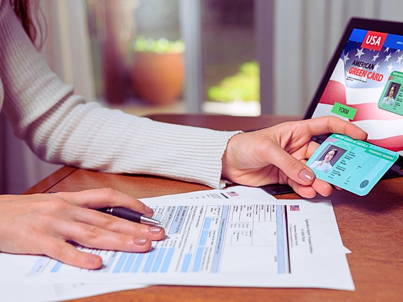 Person holding American Green Card over application forms. travel while your green card renewal is pending